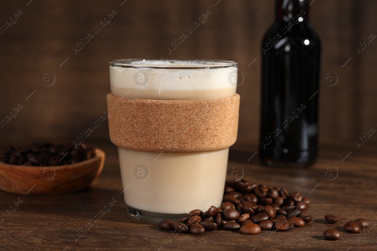Photo of Bottle of delicious syrup, glass of coffee and beans on wooden table, closeup