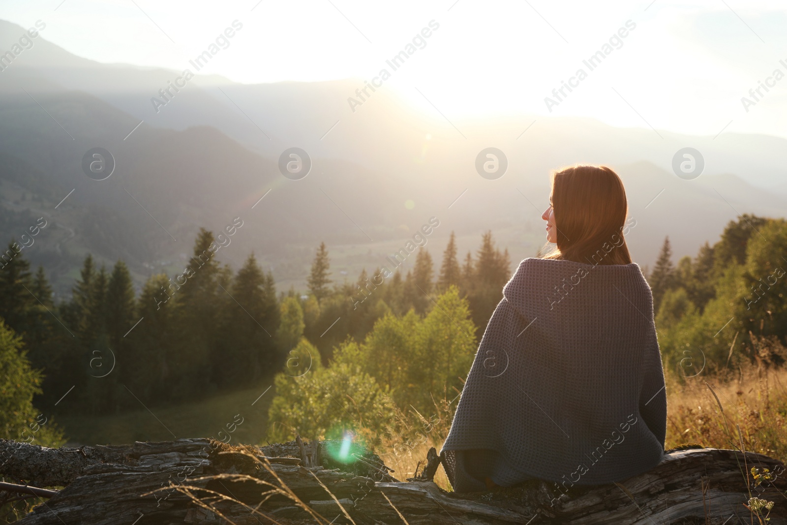 Photo of Woman with cozy plaid enjoying sunset in mountains, back view