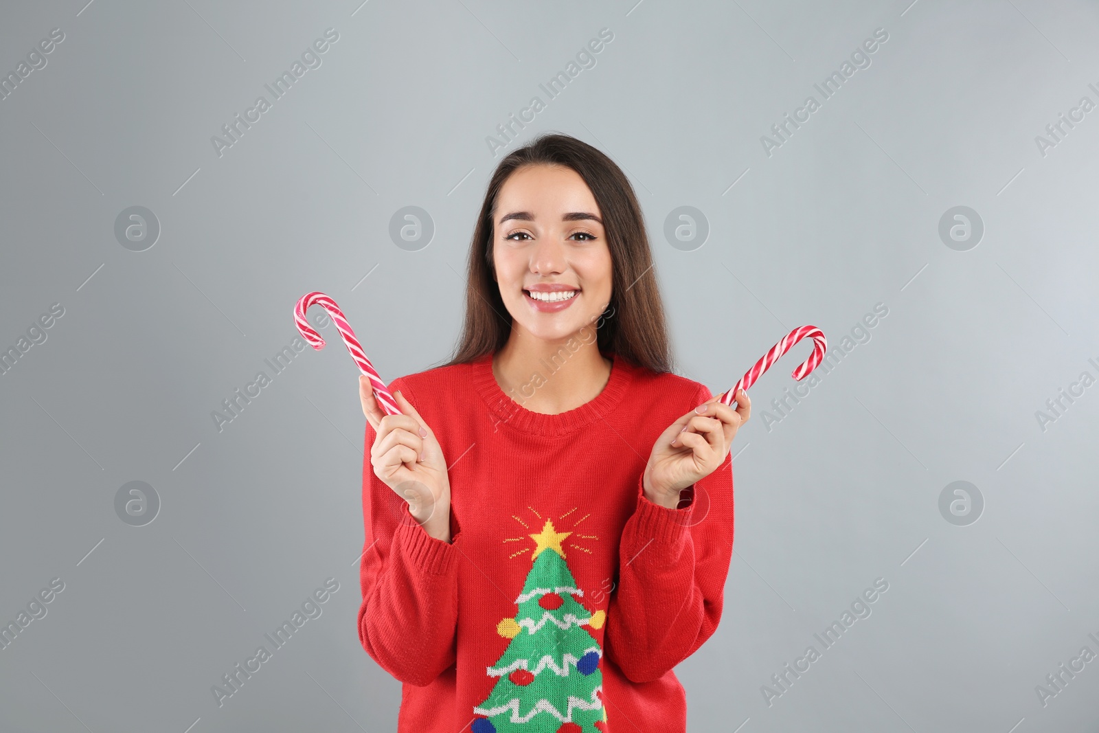 Photo of Young woman in Christmas sweater holding candy canes on grey background