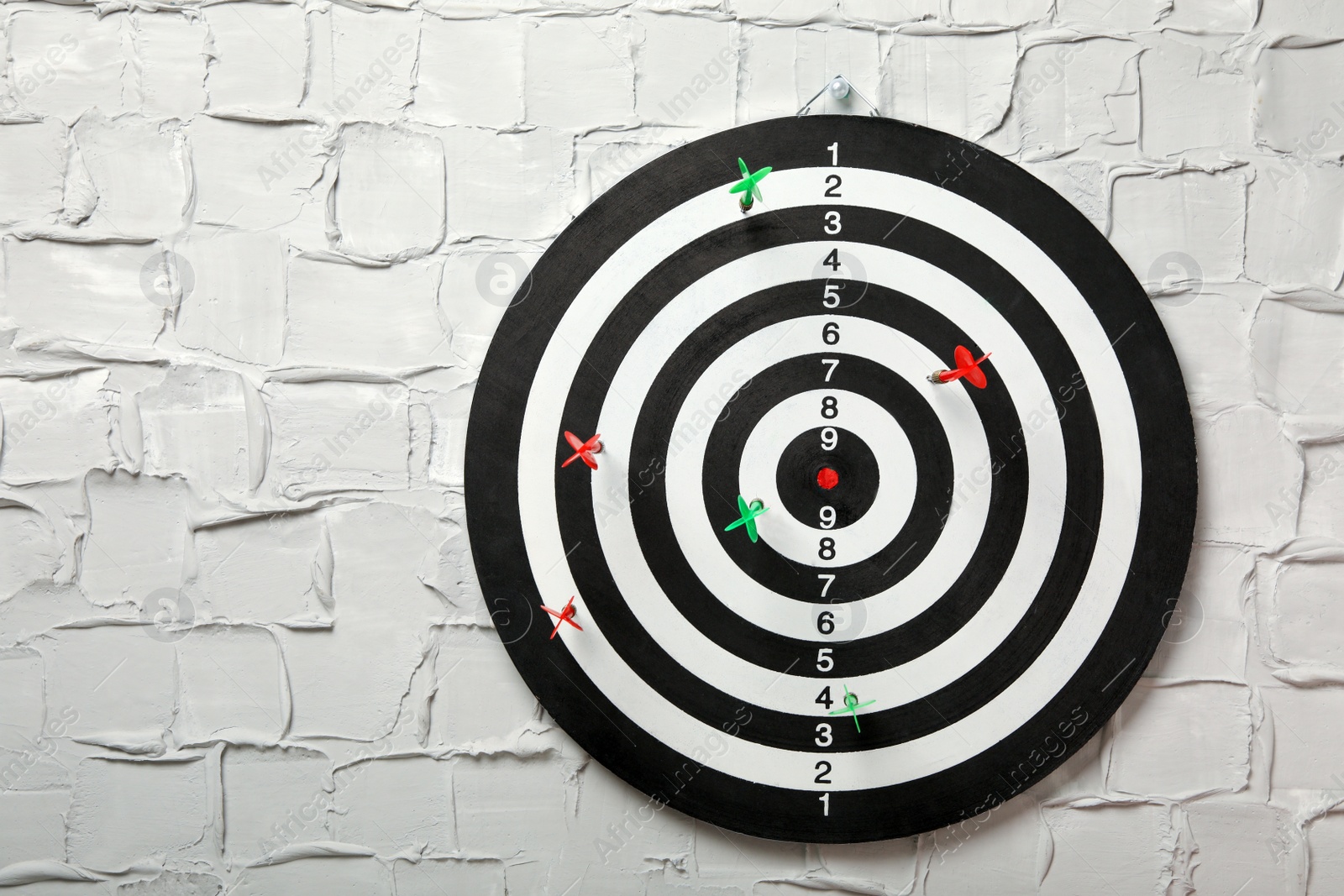 Photo of Arrows hitting dart board on white textured wall. Space for text