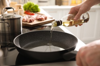 Photo of Man pouring cooking oil into frying pan in kitchen, closeup