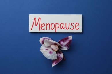 Card with word Menopause and orchid flower on blue background, flat lay