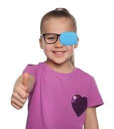 Photo of Girl with eye patch on glasses showing thumb up against white background. Strabismus treatment
