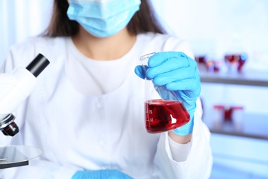 Photo of Laboratory worker with sample in glass flask for analysis, closeup