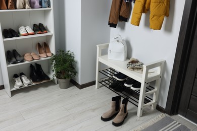 Photo of Shelving unit and shoe storage bench near white wall in hallway. Interior design