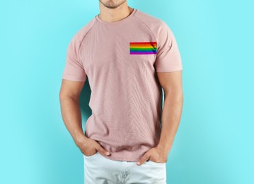 Image of Young man wearing pink t-shirt with image of LGBT pride flag on turquoise background