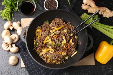 Photo of Stir-fry. Tasty noodles with meat and vegetables in wok served on dark textured table, flat lay