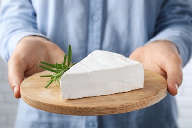 Woman holding serving board with delicious brie cheese on blurred background, closeup