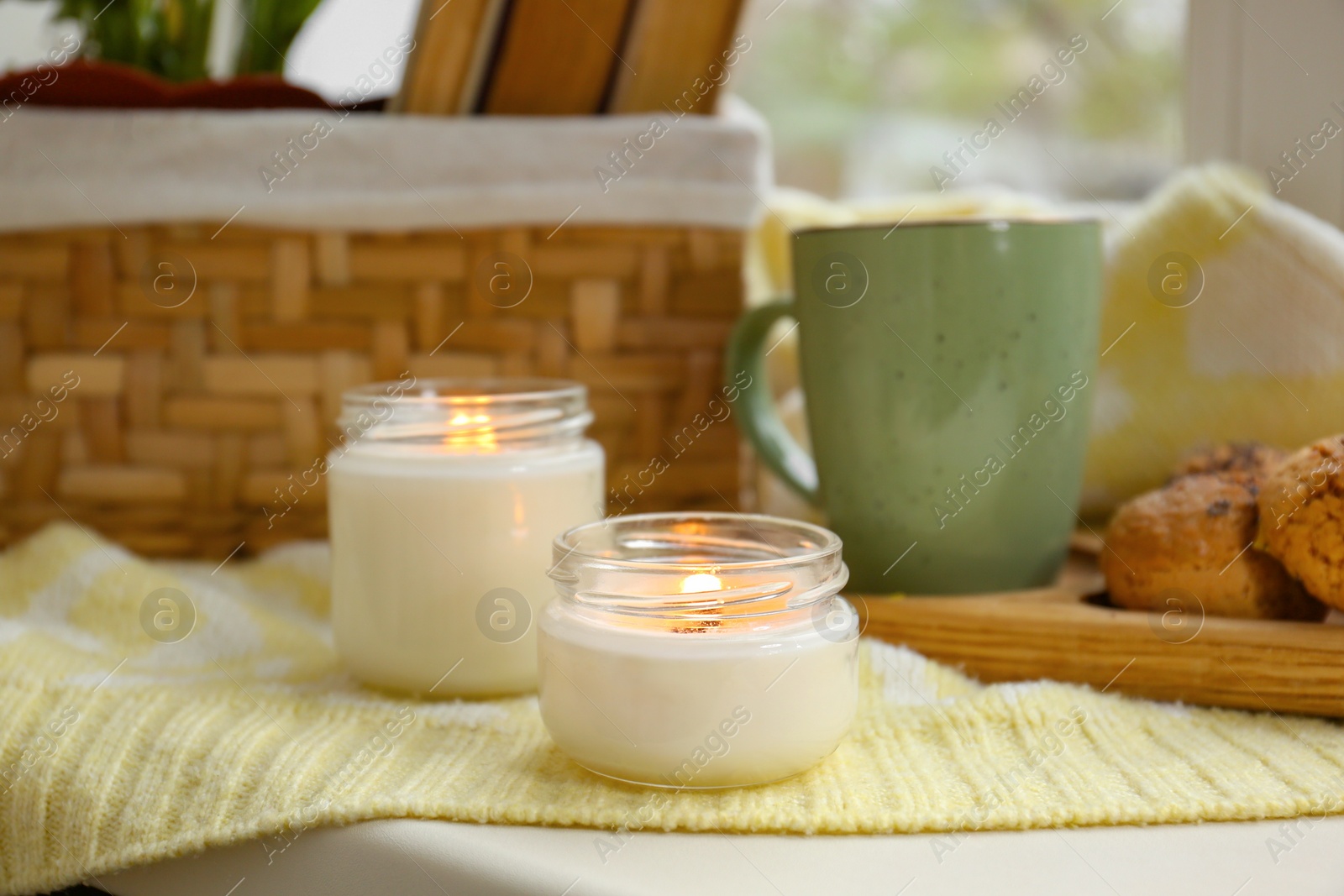 Photo of Burning aromatic candles, cup with hot drink on table indoors. Autumn coziness