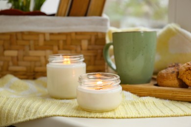 Photo of Burning aromatic candles, cup with hot drink on table indoors. Autumn coziness