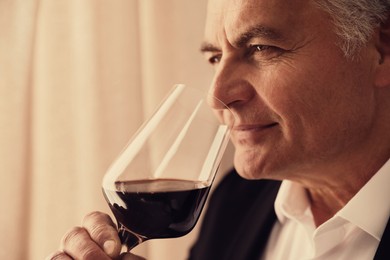 Senior man with glass of red wine indoors