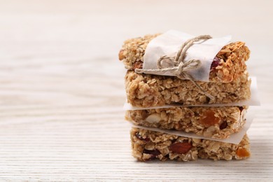Stack of tasty granola bars on white wooden table, closeup. Space for text