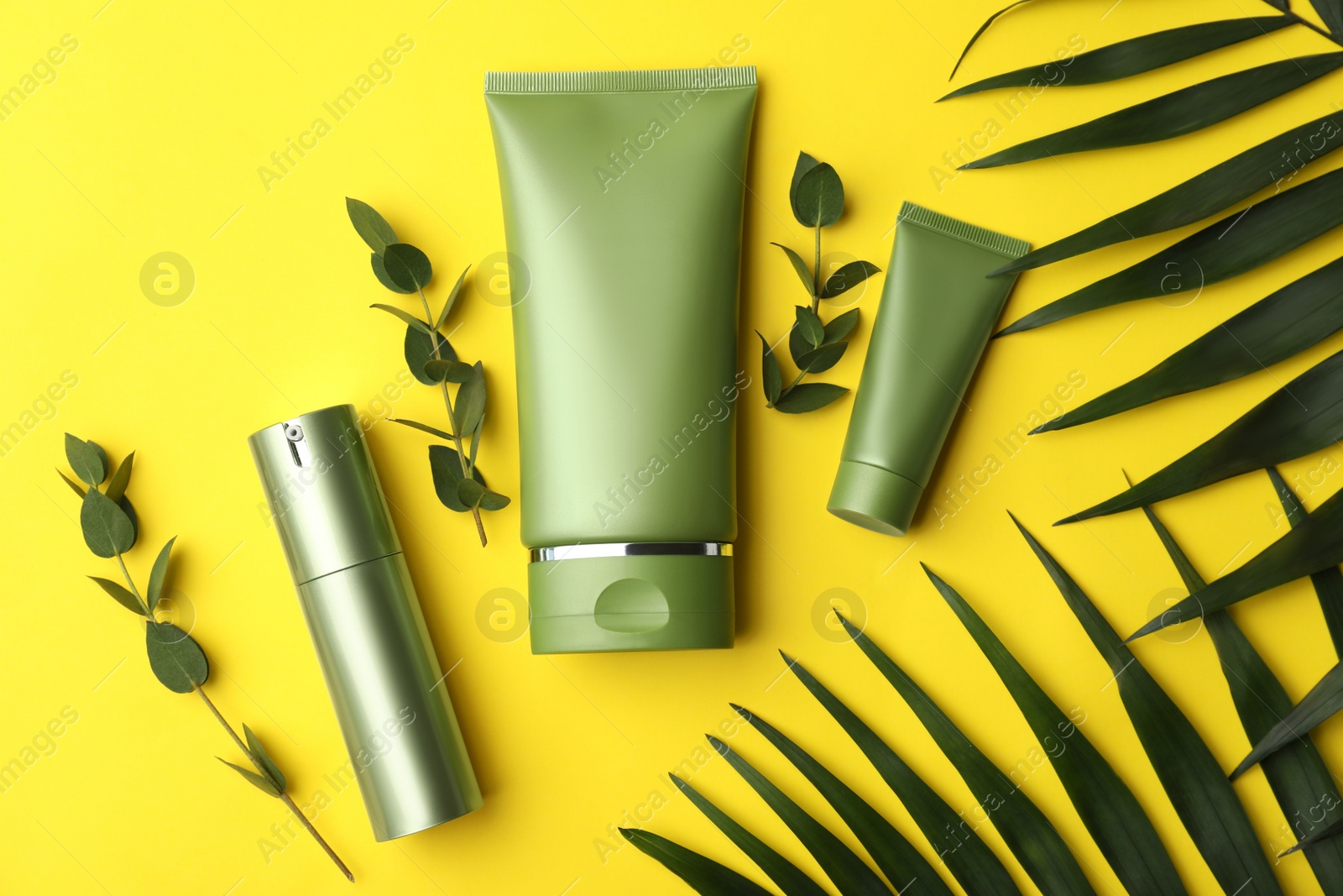 Photo of Set of cosmetic products and green leaves on yellow background, flat lay