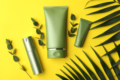 Photo of Set of cosmetic products and green leaves on yellow background, flat lay