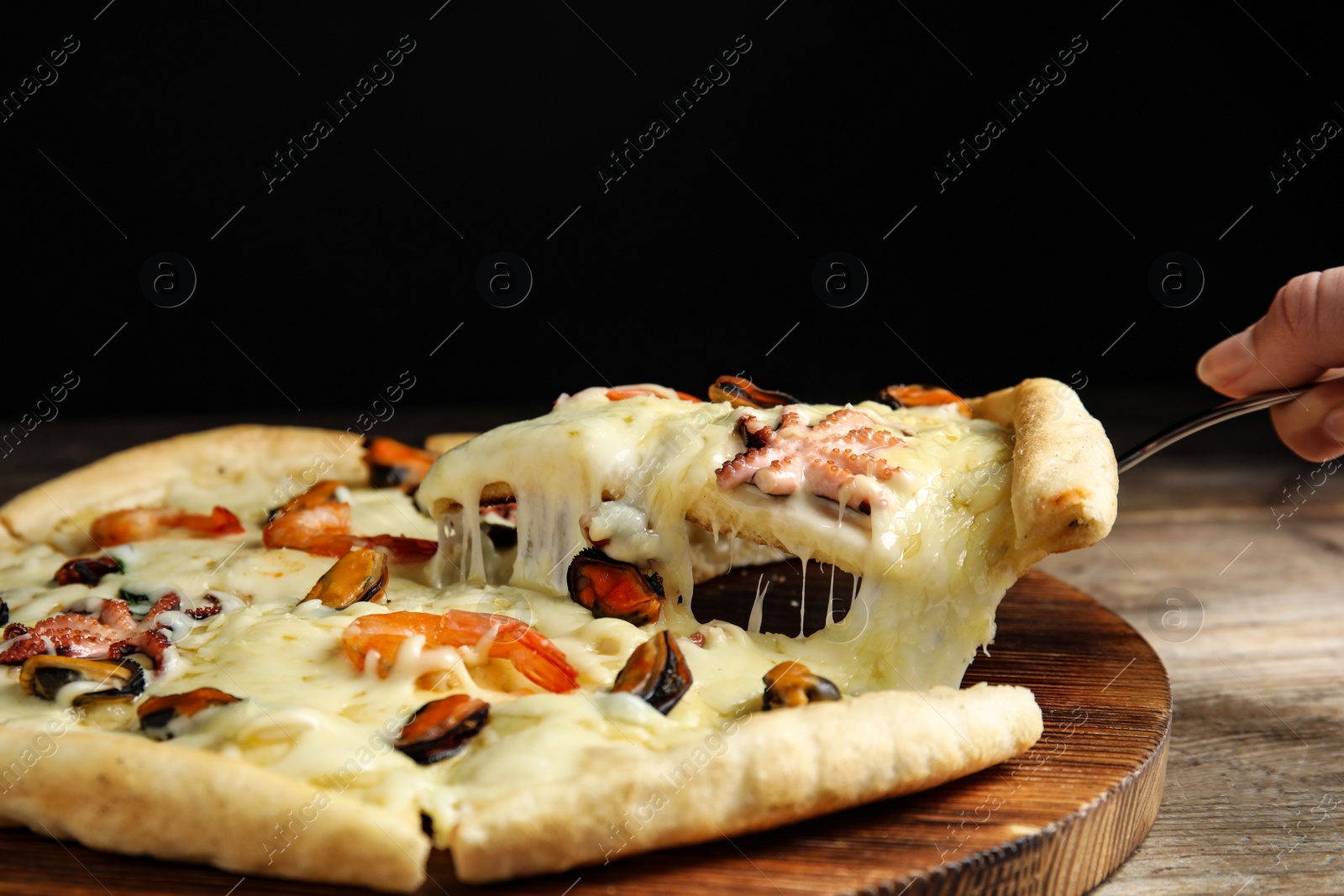 Photo of Woman taking piece of delicious seafood pizza at wooden table, closeup