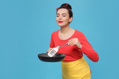 Housewife with frying pan and spatula on light blue background