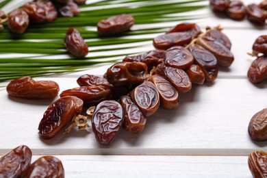 Sweet dried dates with palm leaf on white wooden table, closeup