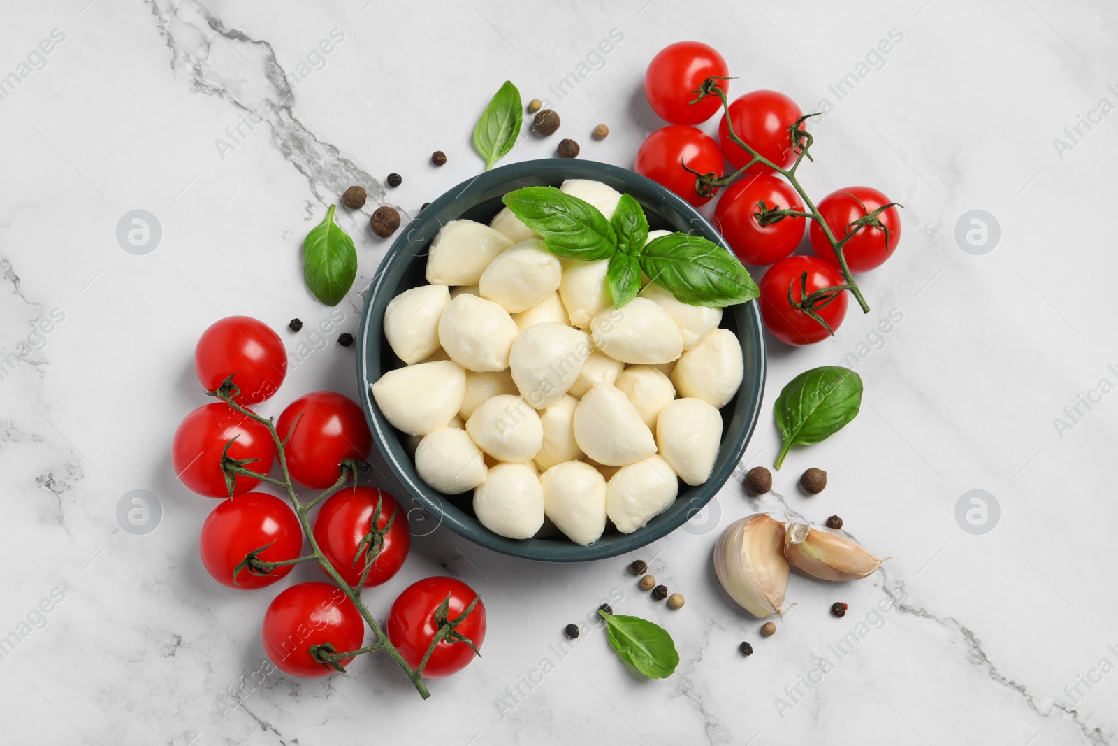Photo of Delicious mozzarella balls in bowl, tomatoes and basil leaves on white marble table, flat lay