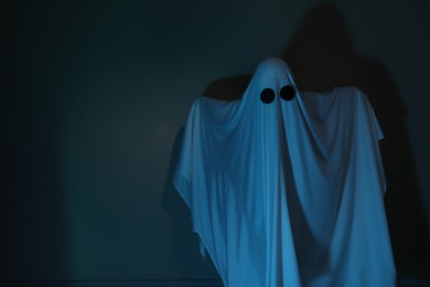 Photo of Creepy ghost. Woman covered with sheet in color light, space for text