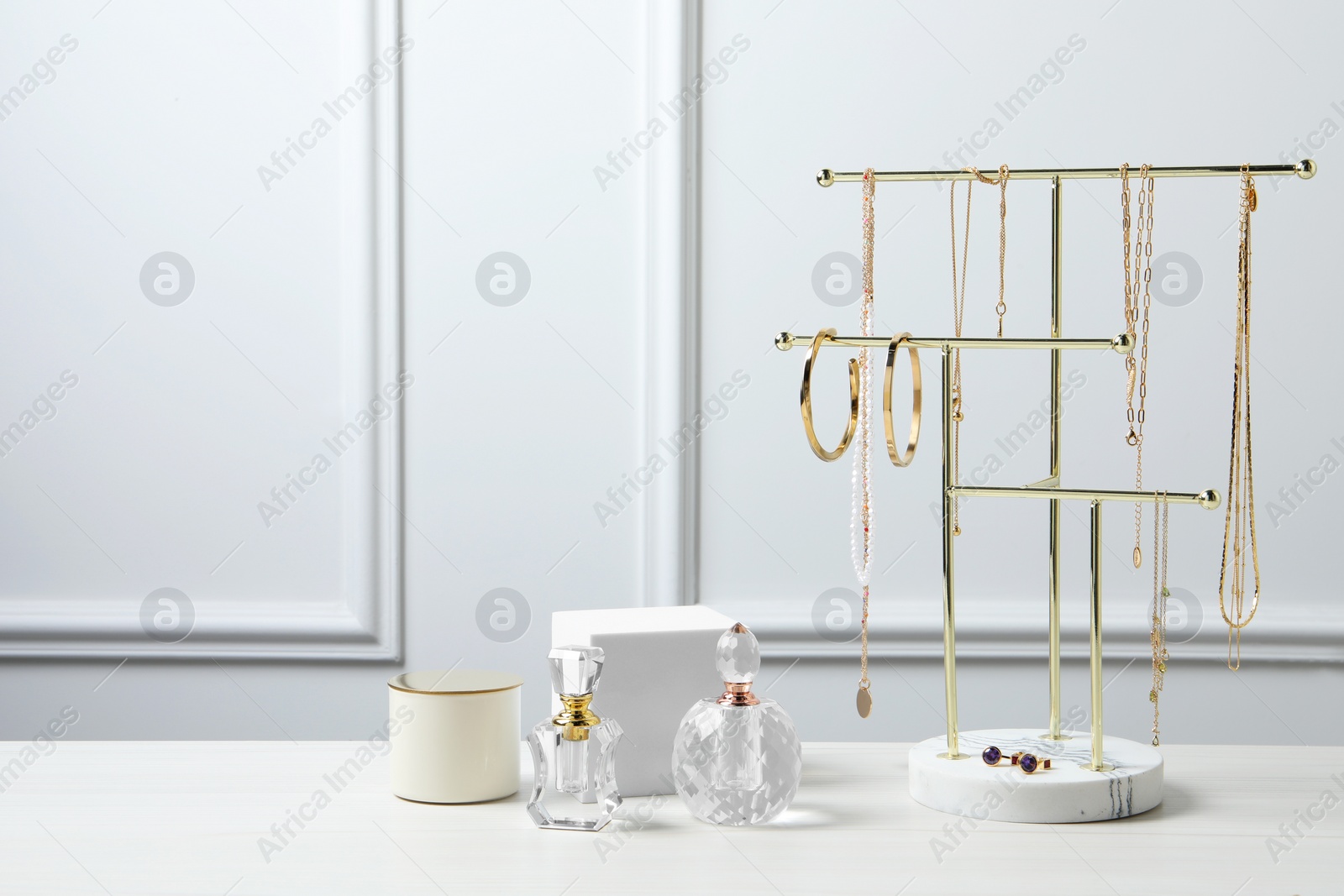 Photo of Holder with set of beautiful bijouterie and perfume bottles on white wooden table, space for text