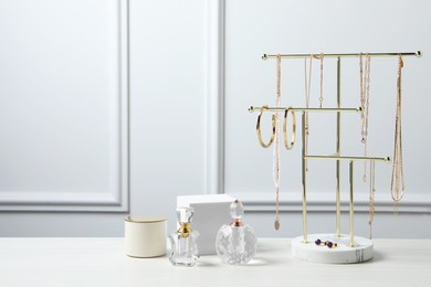 Photo of Holder with set of beautiful bijouterie and perfume bottles on white wooden table, space for text