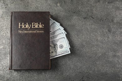 Photo of Holy Bible and money on grey table, top view. Space for text