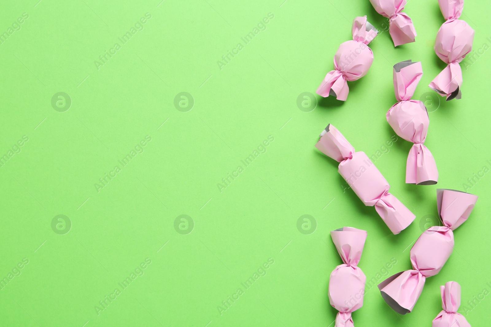 Photo of Many candies in light pink wrappers on green background, flat lay. Space for text