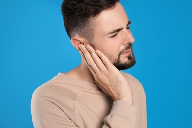 Young man suffering from ear pain on light blue background