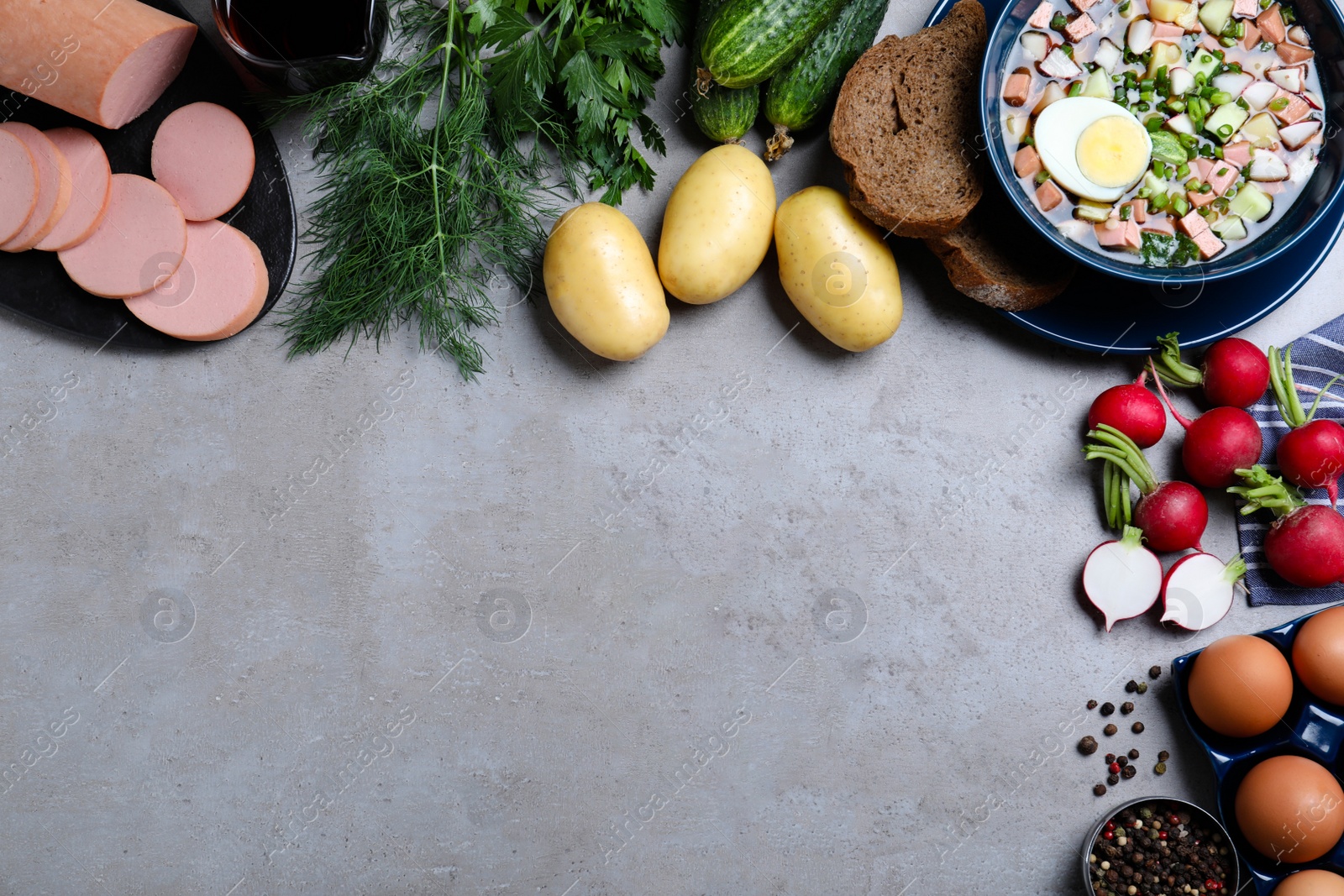 Photo of Flat lay composition of cold okroshka with kvass and other ingredients on grey table, space for text. Traditional Russian summer soup