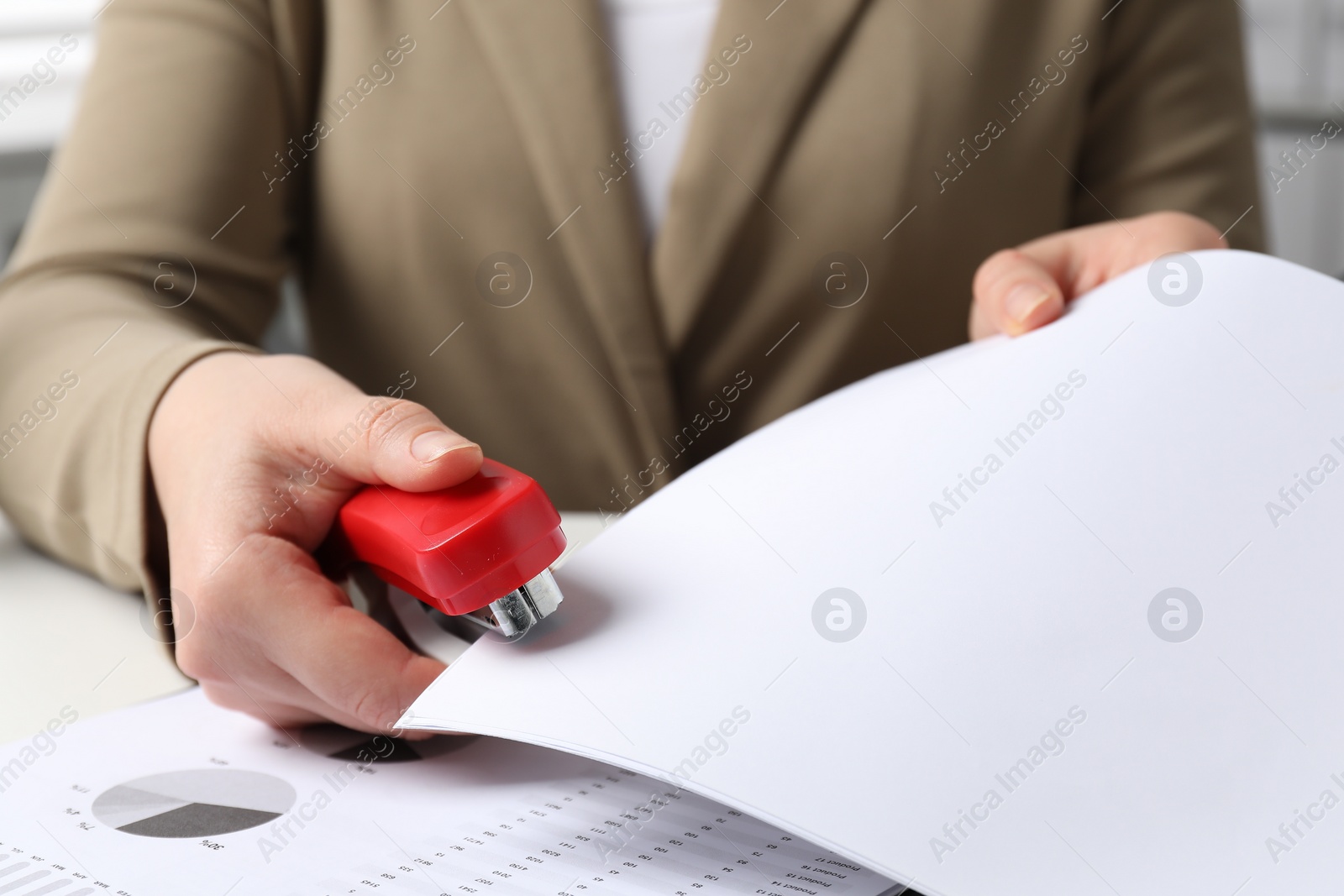 Photo of Woman with papers using stapler at white table, closeup