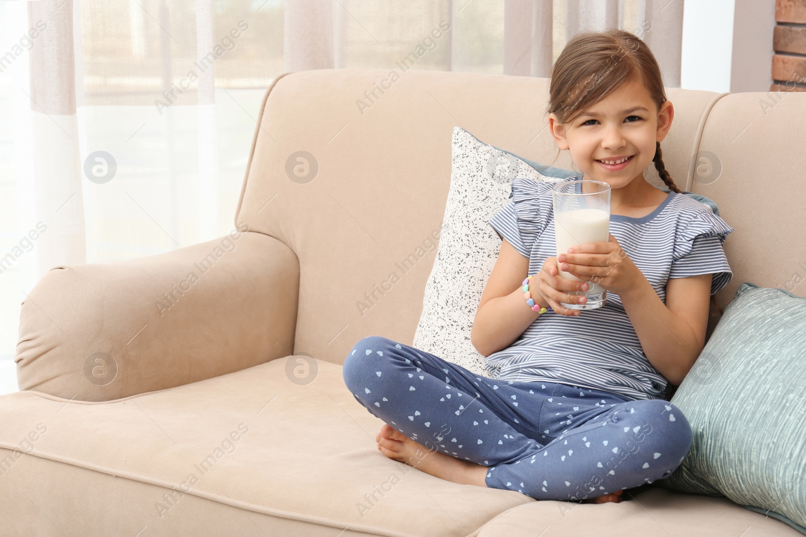 Photo of Cute little girl with glass of milk on sofa at home