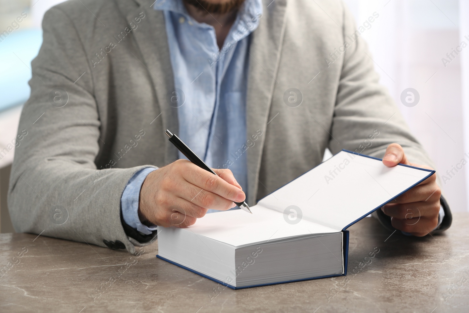 Photo of Writer signing autograph in book at table, closeup