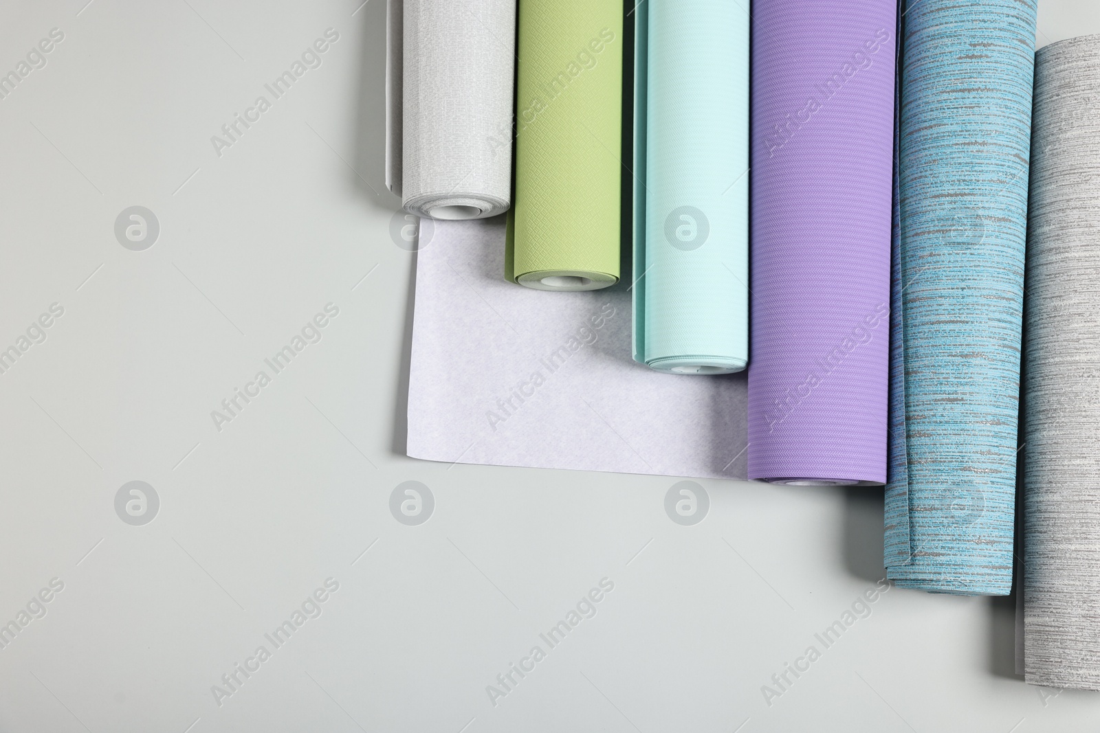 Photo of Different wallpaper rolls on light background, flat lay. Space for text