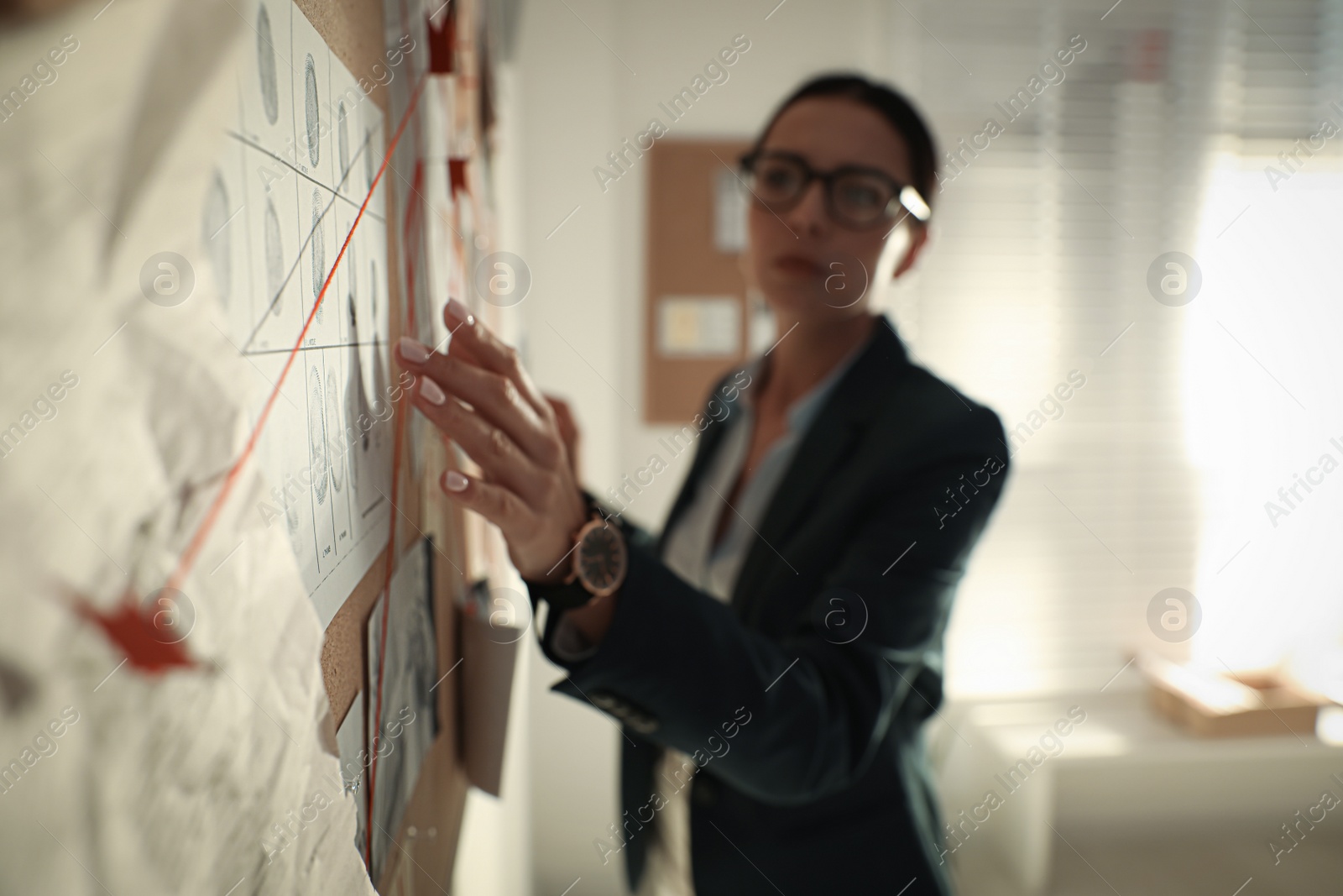 Photo of Detective looking at evidence board in office, focus on hand