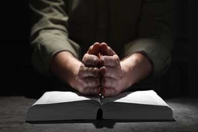 Photo of Religion. Christian man praying over Bible at table, closeup