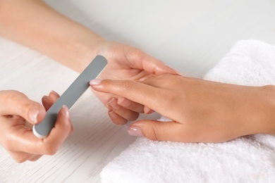 Photo of Manicurist filing client's nails at table, closeup. Spa treatment