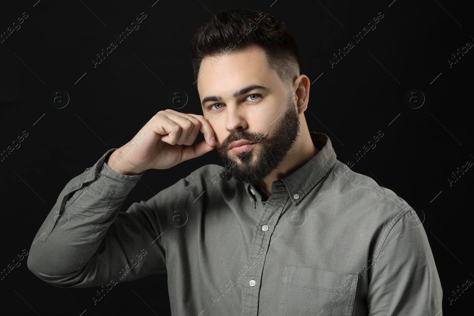 Photo of Young man in shirt touching mustache on black background