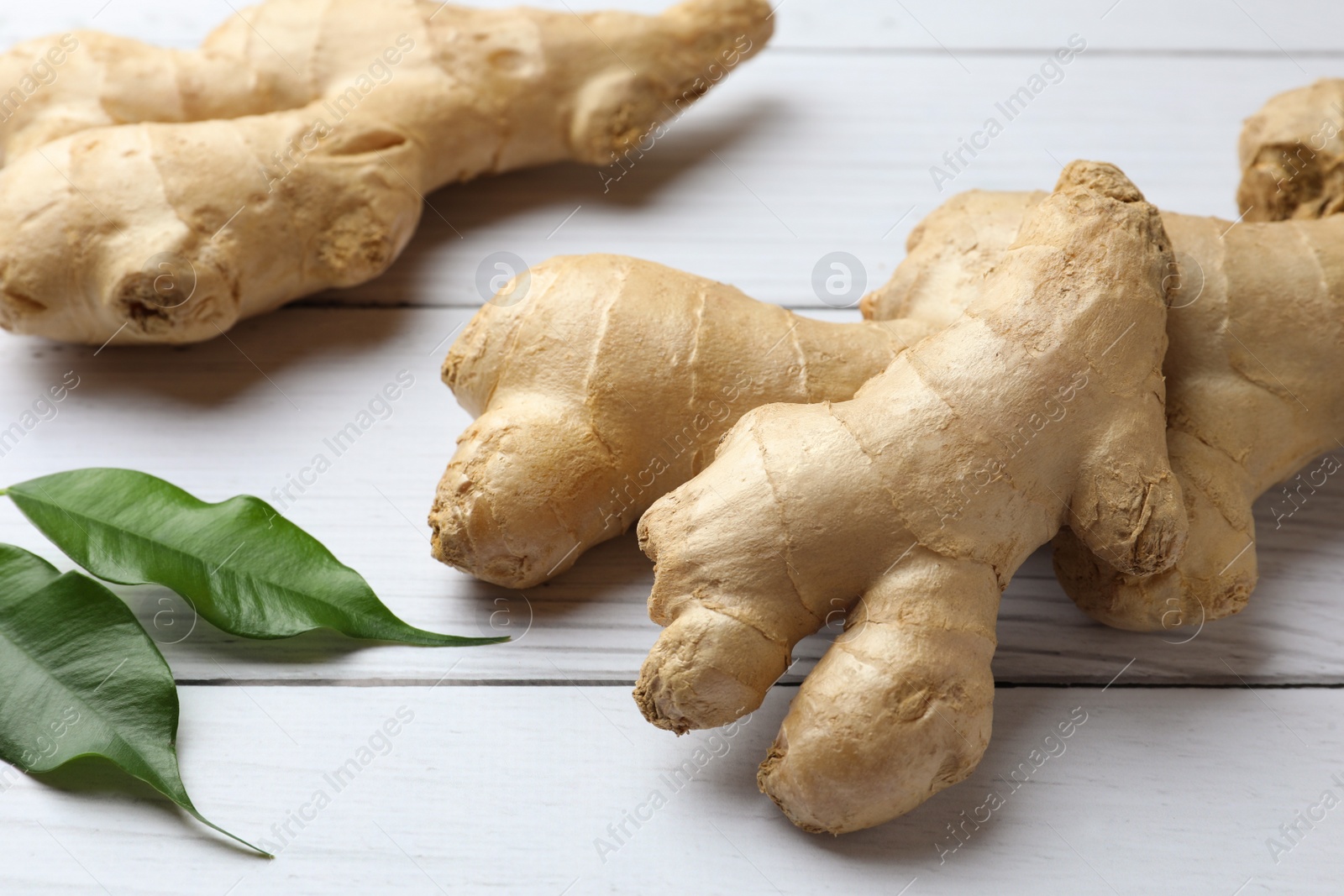 Photo of Fresh ginger with leaves on white wooden table, closeup