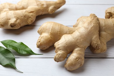 Fresh ginger with leaves on white wooden table, closeup