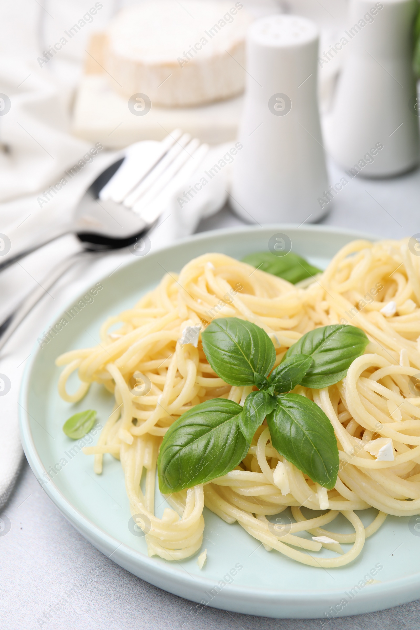 Photo of Delicious pasta with brie cheese and basil leaves on light grey table, closeup. Space for text