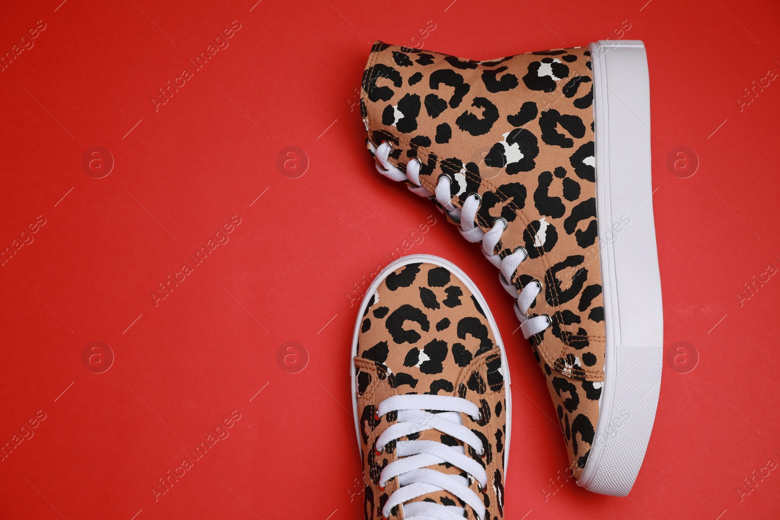 Photo of Pair of classic old school sneakers with leopard print on red background, flat lay. Space for text