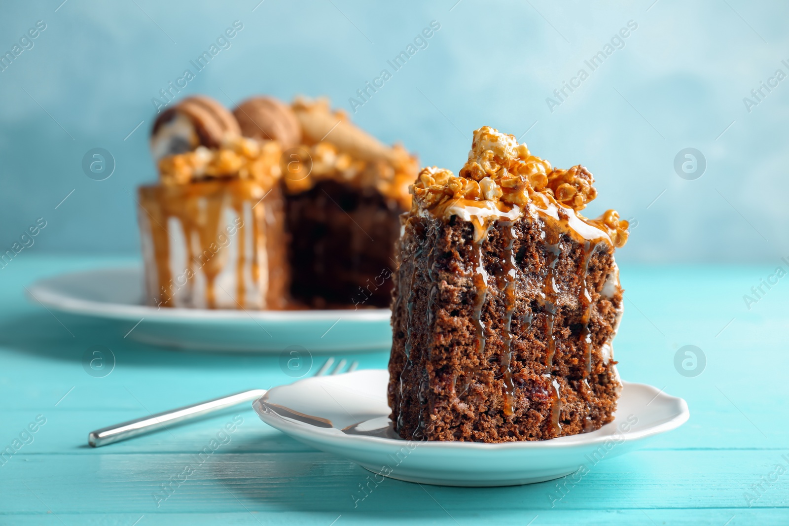 Photo of Piece of delicious homemade cake with caramel sauce and popcorn on table