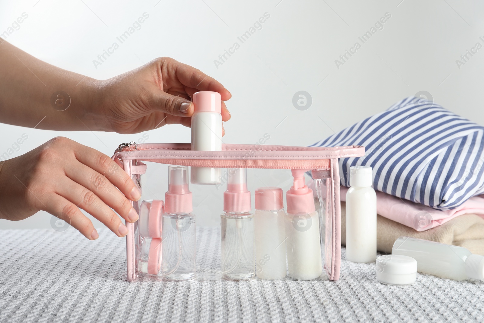 Photo of Woman putting small bottle with personal care product into plastic bag, closeup. Cosmetic travel kit