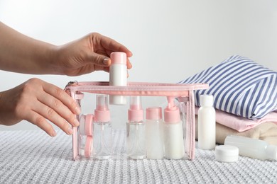 Woman putting small bottle with personal care product into plastic bag, closeup. Cosmetic travel kit