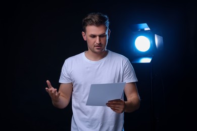 Casting call. Emotional man with script performing on black background