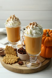 Photo of Tasty pumpkin latte with whipped cream in glasses, spices and cookies on white wooden table