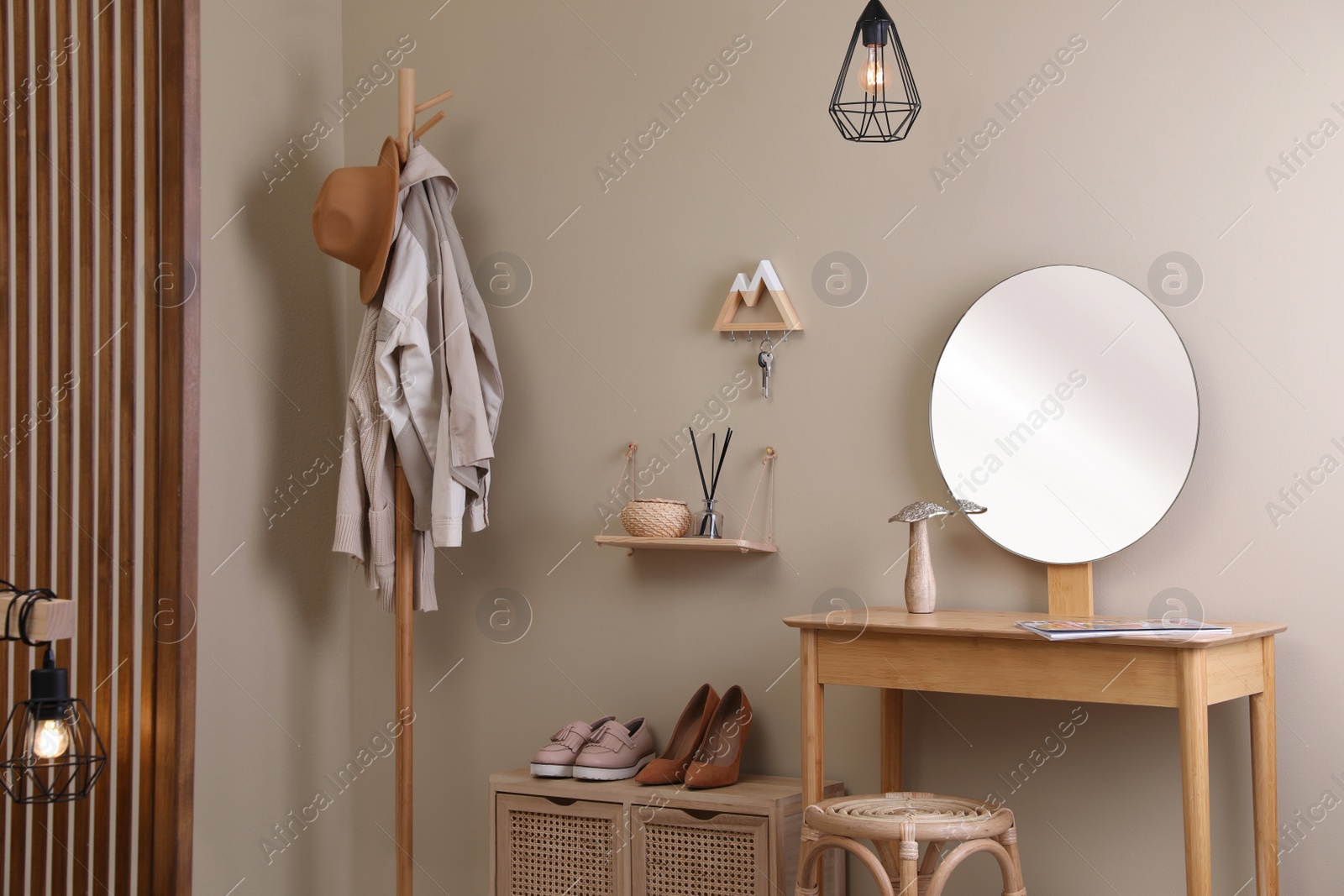 Photo of Modern hallway interior with stylish furniture, round mirror and wooden hanger for keys on beige wall