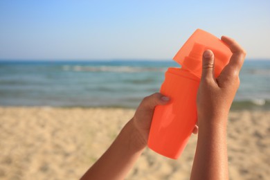 Photo of Child with bottle of sunscreen near sea, closeup. Space for text. Sun protection care