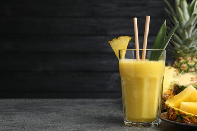 Tasty pineapple smoothie and fruit on grey table. Space for text