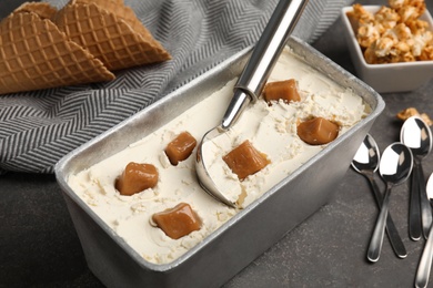 Delicious ice cream in container with caramel on table